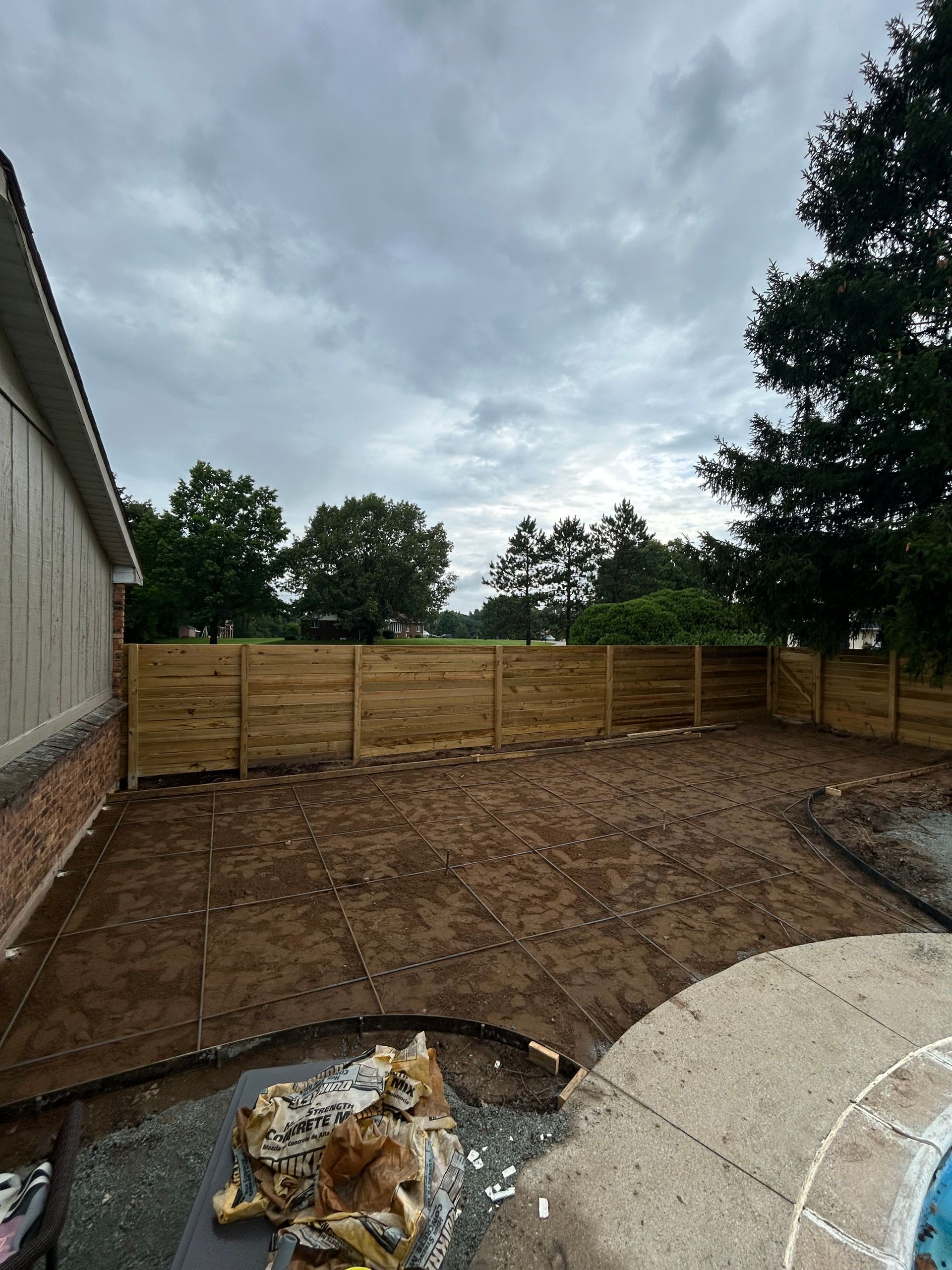 A backyard with a wooden fence and freshly turned soil, under a cloudy sky.