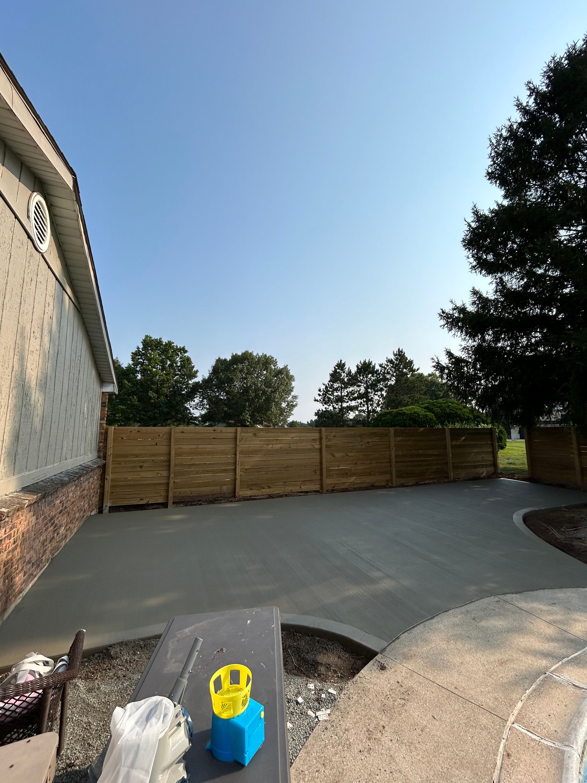 Concrete patio next to a house and a wooden fence under a clear sky.