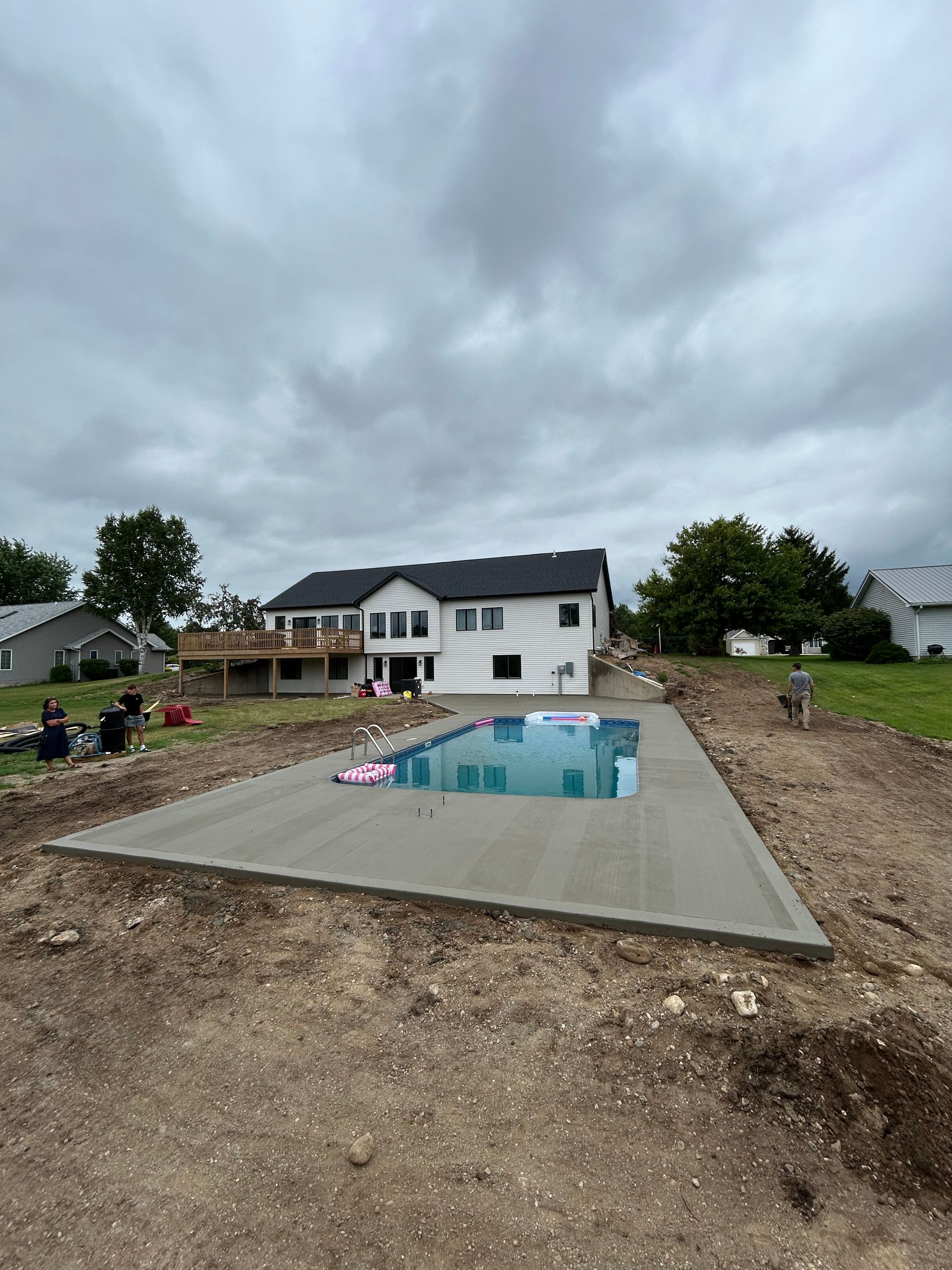 Backyard construction with a partially built pool in front of a two-story house.