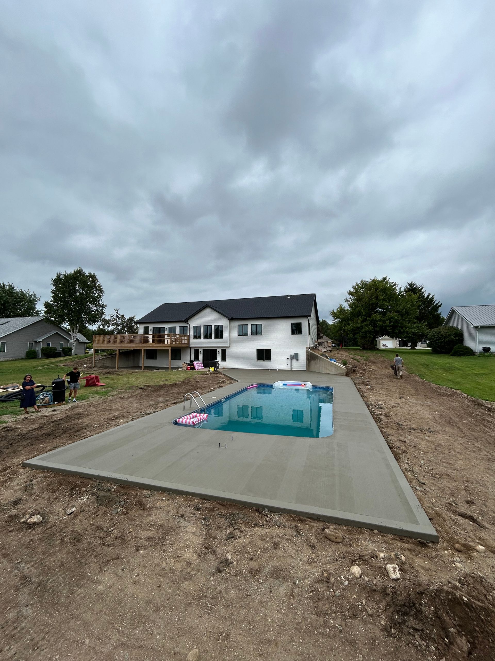 A two-story white house with a new pool under a cloudy sky.