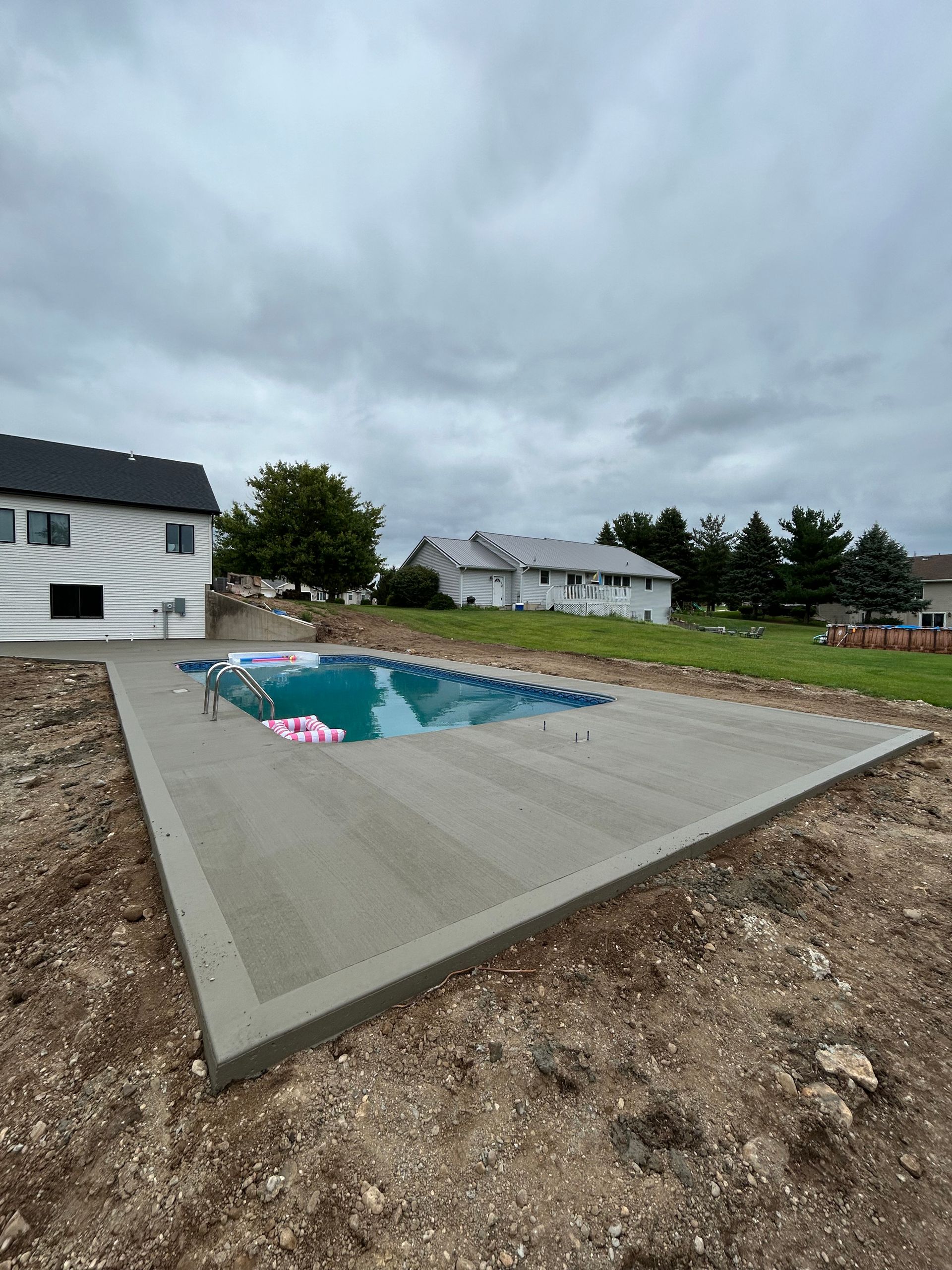 Newly constructed rectangular pool with concrete patio in a grassy yard.