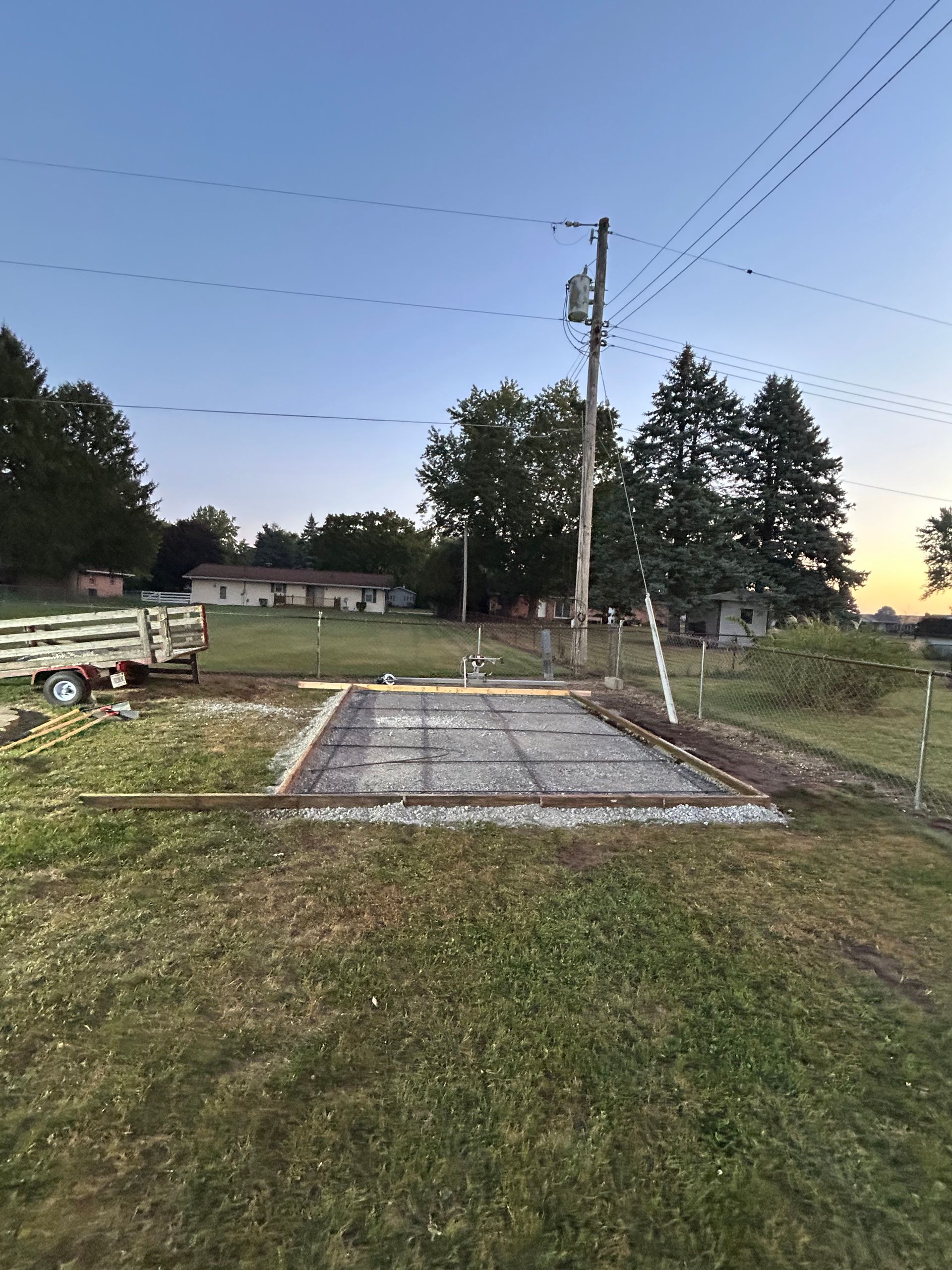 Concrete foundation set for a building in a grassy field, with power lines and trees in the background.