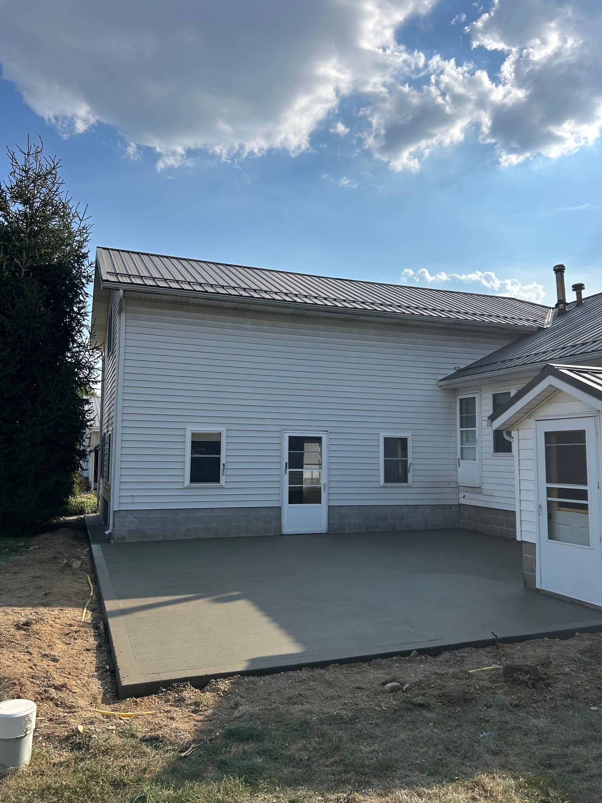 White house with gray roof and newly poured concrete patio under a blue sky.