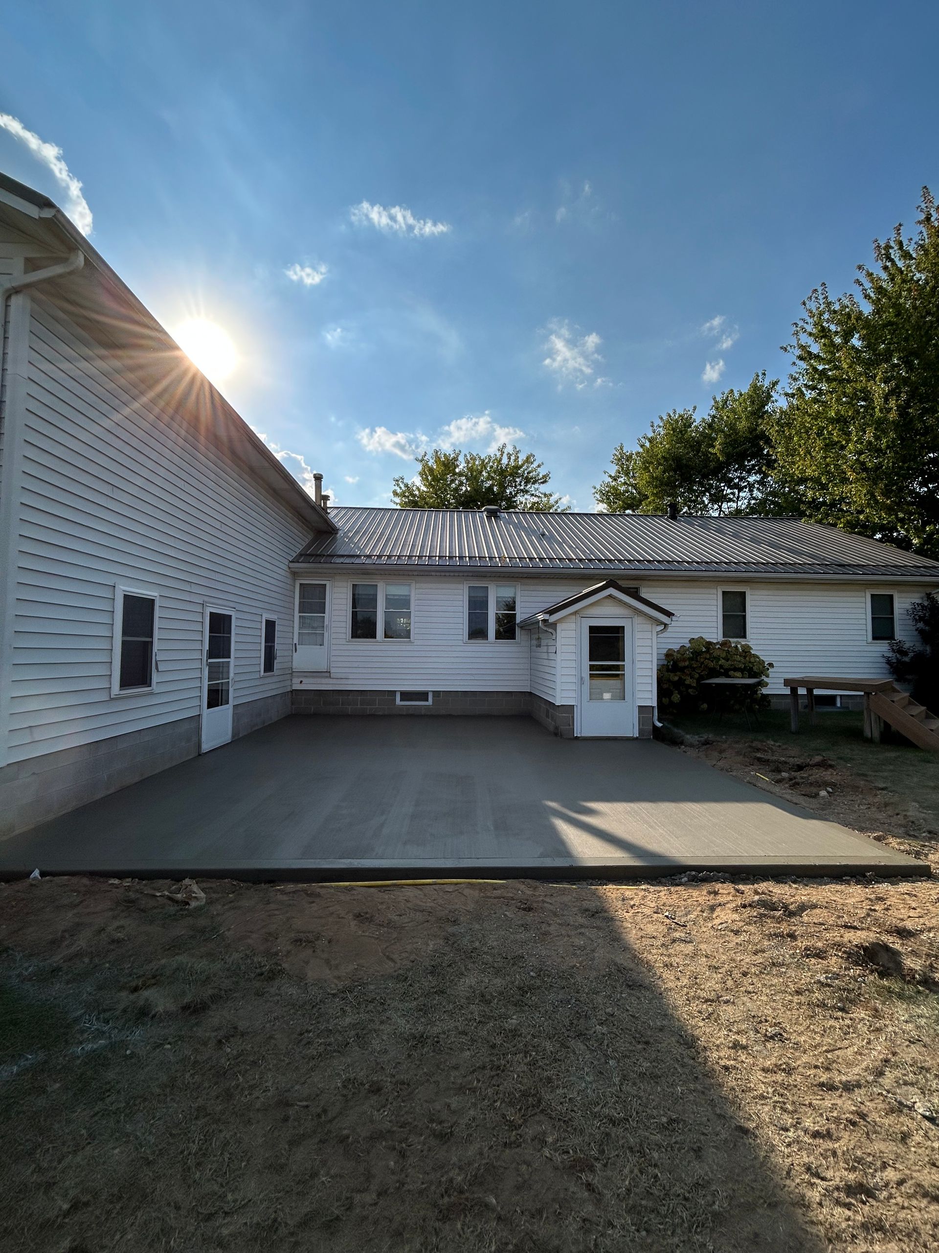 White farmhouse with a sunlit driveway, under a blue sky.