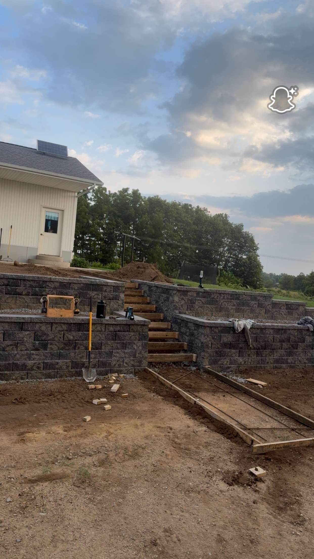 Stone retaining walls with stairs lead up to a house under construction against a cloudy sky.