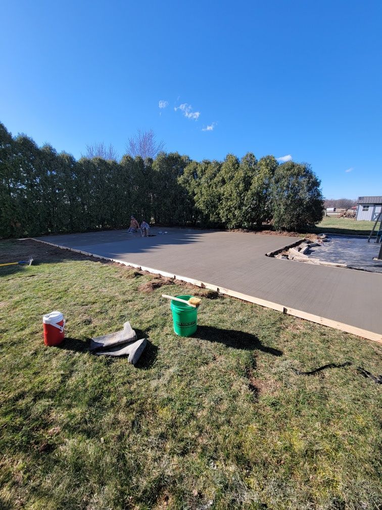 Newly poured concrete patio in a backyard, with tools and green grass.