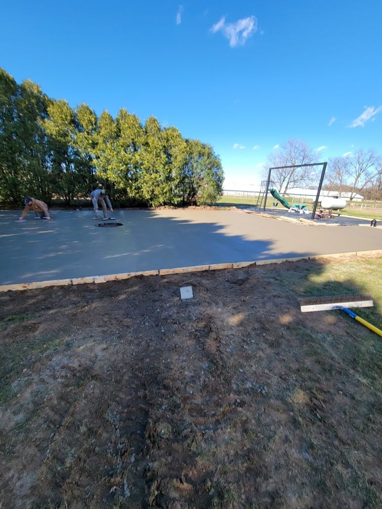 Two people smoothing wet concrete in a backyard, a swing set in the background.