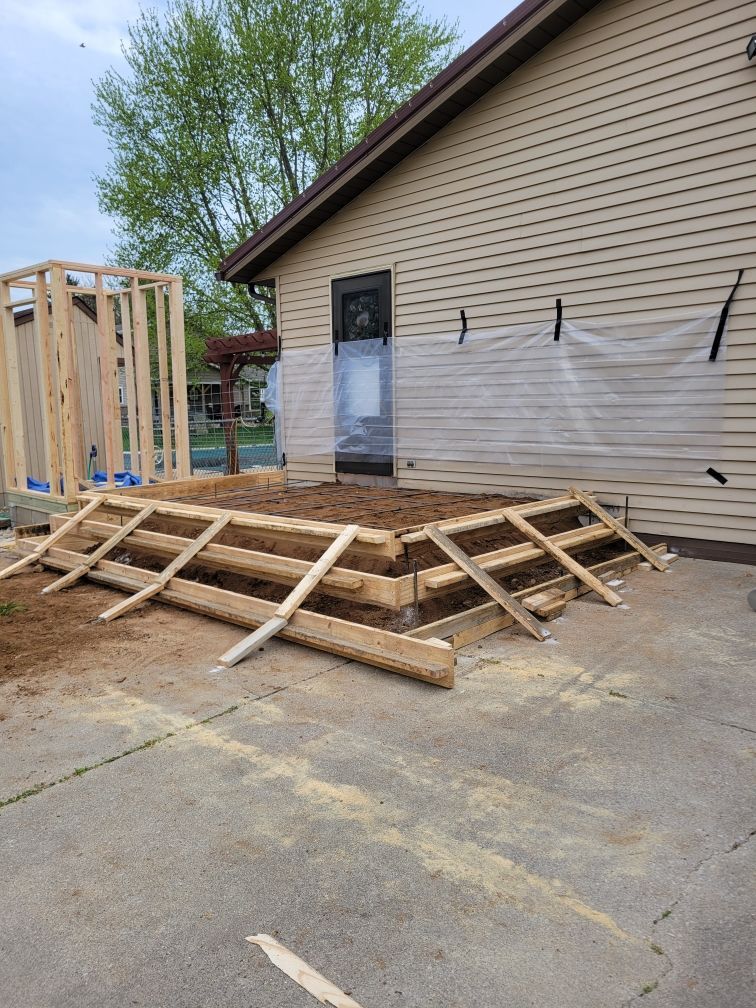 Wooden deck under construction next to a tan building. Sawdust on the ground.