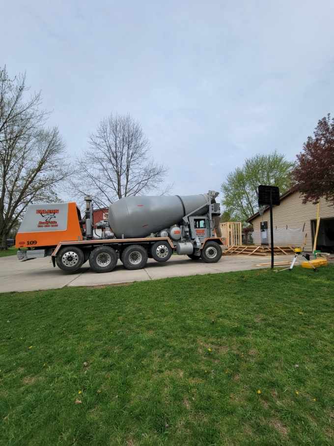 Cement truck parked on a residential driveway; delivering concrete for a construction project near a garage.
