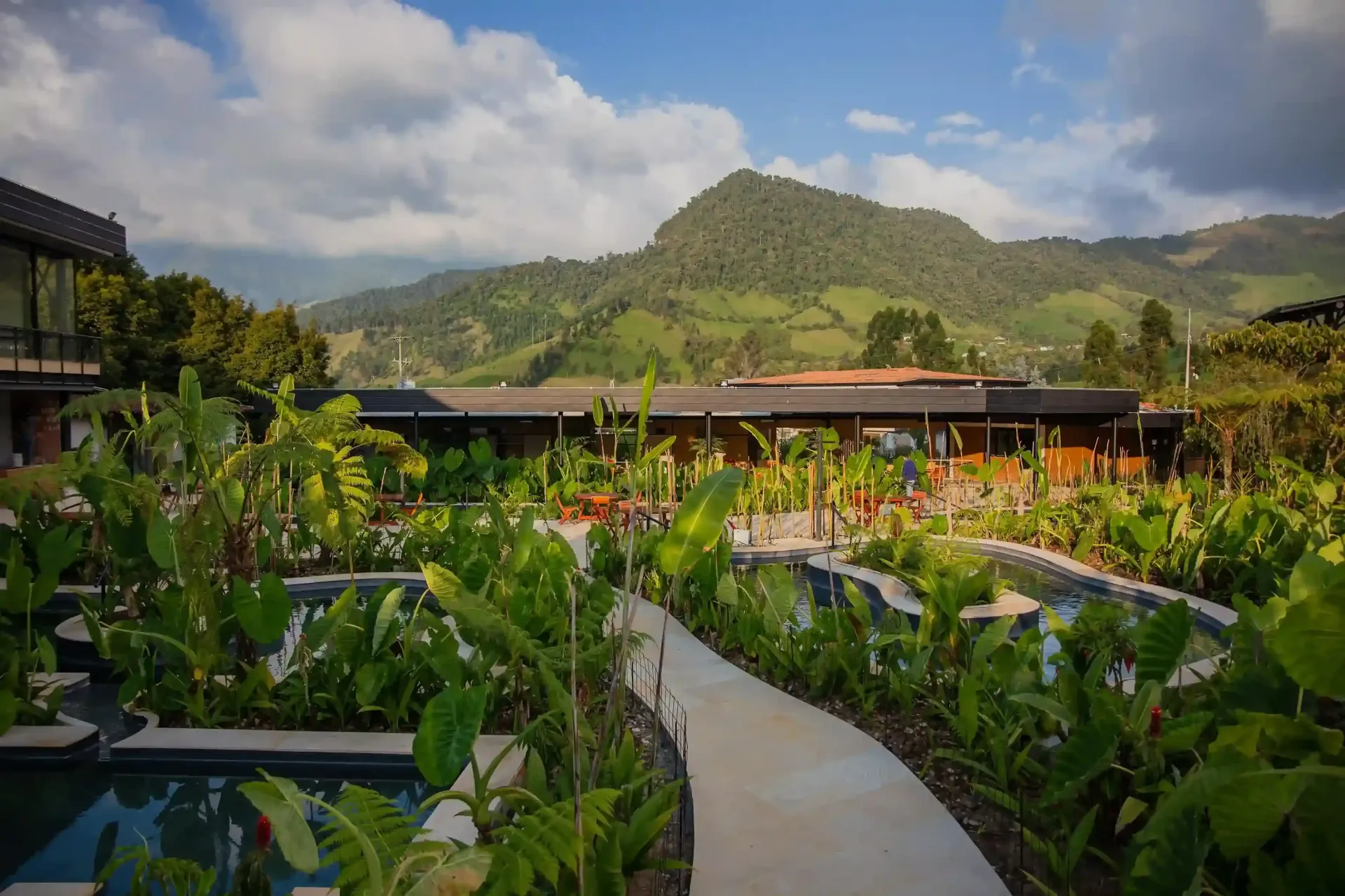 Jardines y senderos rodeados de naturaleza en el Hotel Termales El Otoño, con vegetación tropical, piscinas termales y vista a las montañas cerca de Manizales.