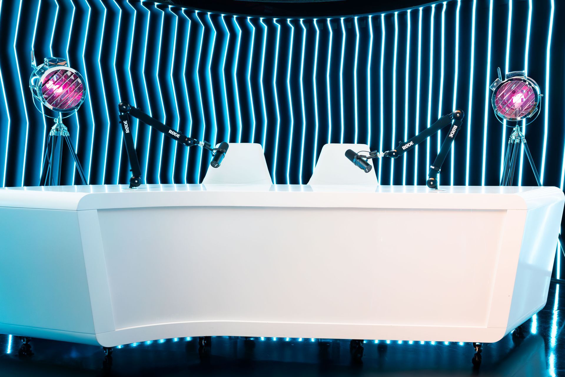 A white desk with two microphones on it in front of a striped wall.