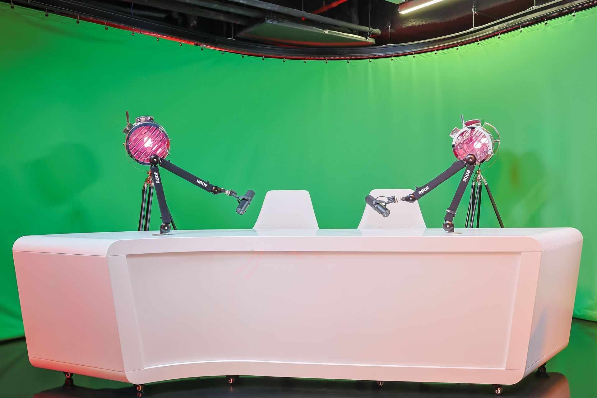 Two robots are standing on top of a white desk in front of a green screen.