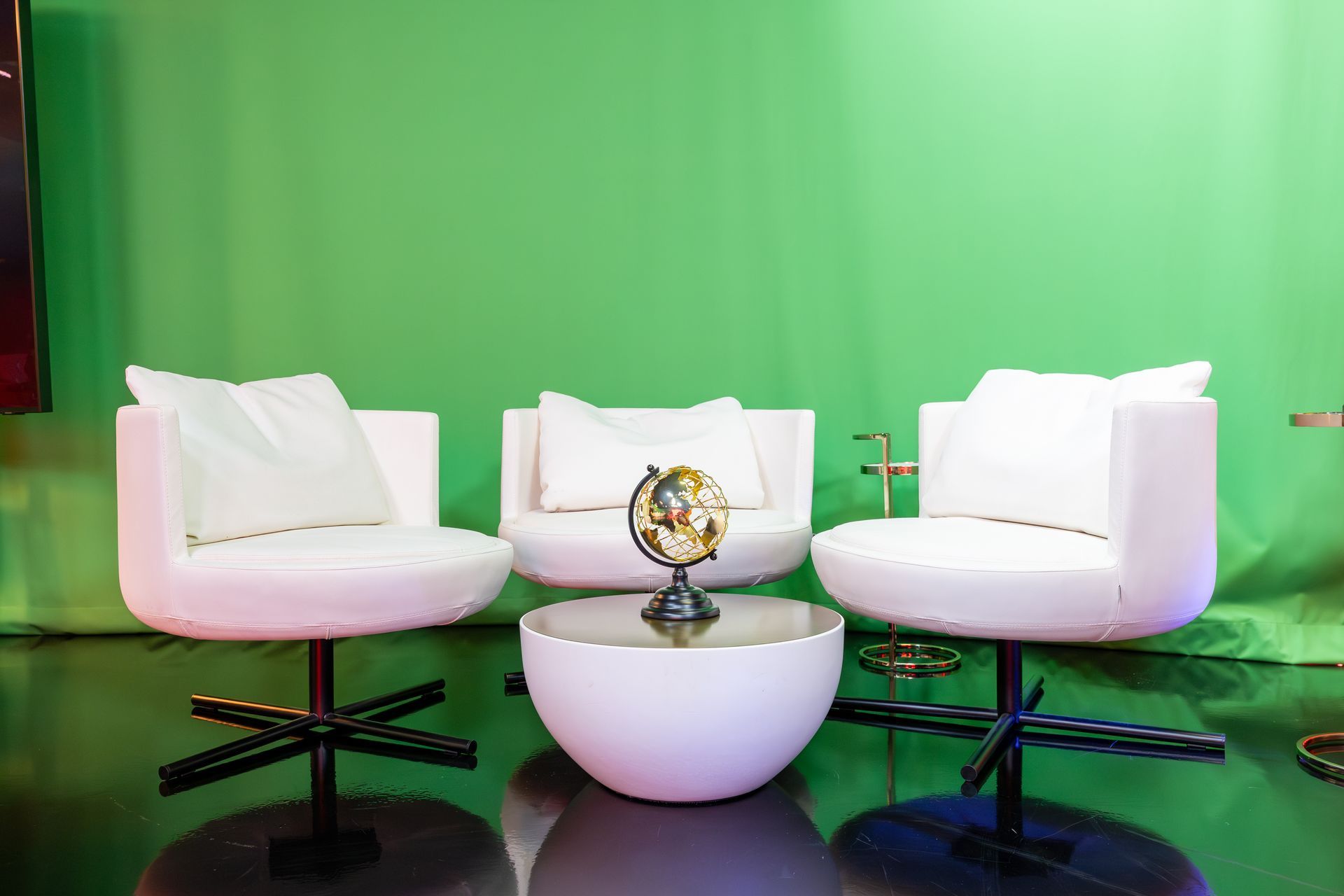 There are three chairs and a table in front of a green screen.