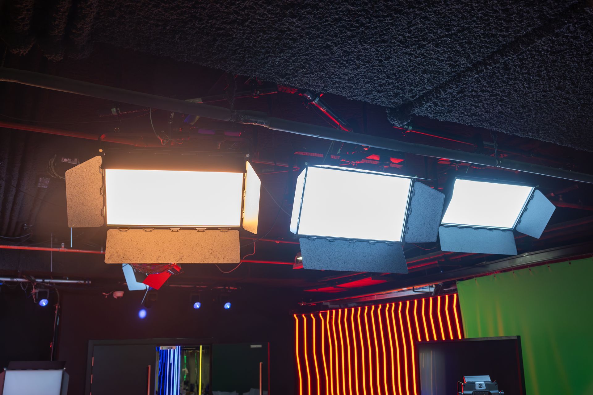 A room with a green screen and a lot of lights hanging from the ceiling.