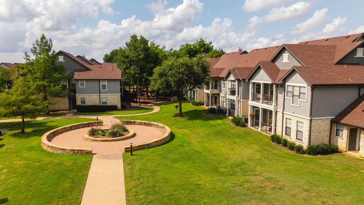 Aerial view of townhouse-style apartment buildings surrounding a circular brick plaza with greenery.