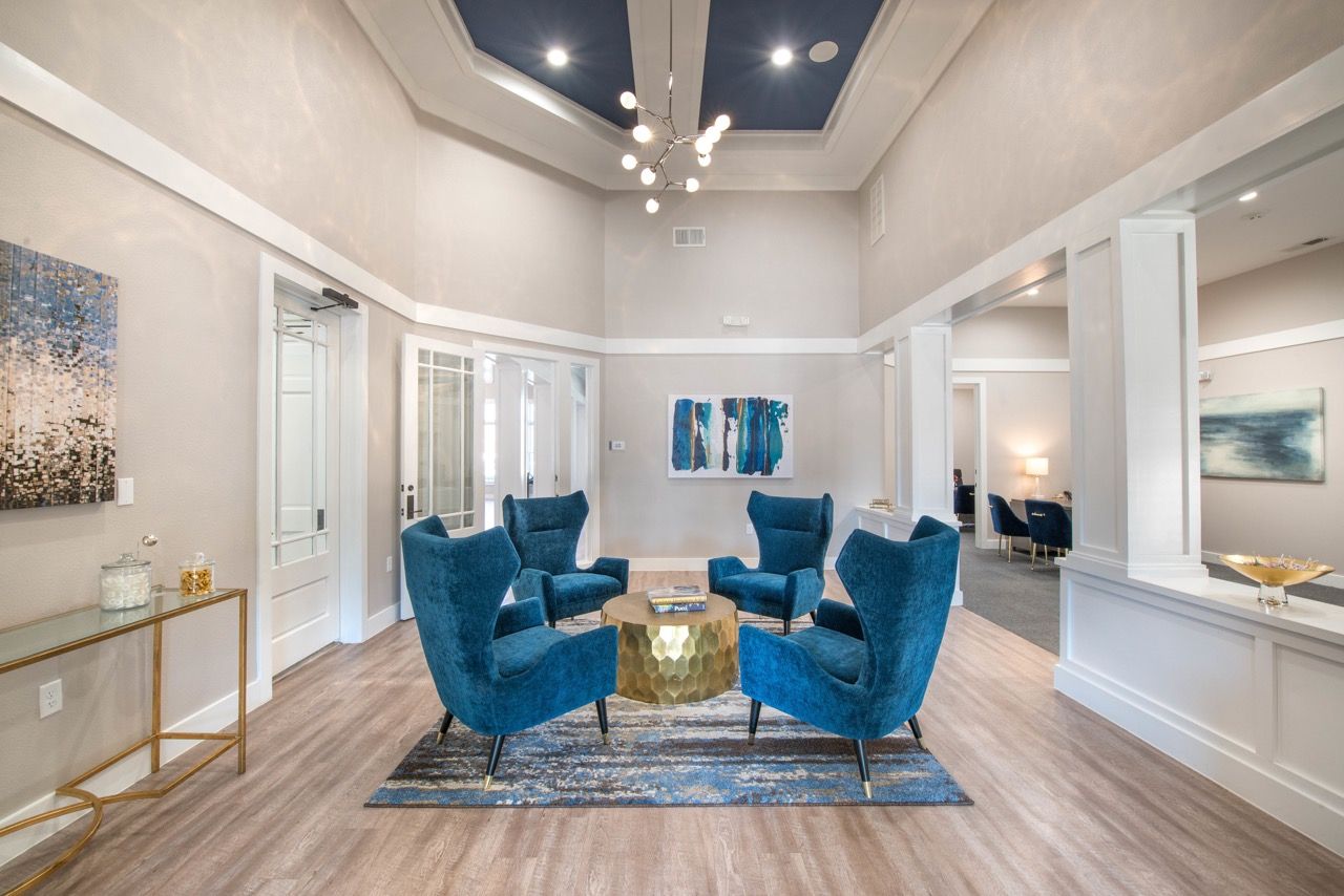 Interior community lounge with six blue chairs around a gold hexagonal coffee table.