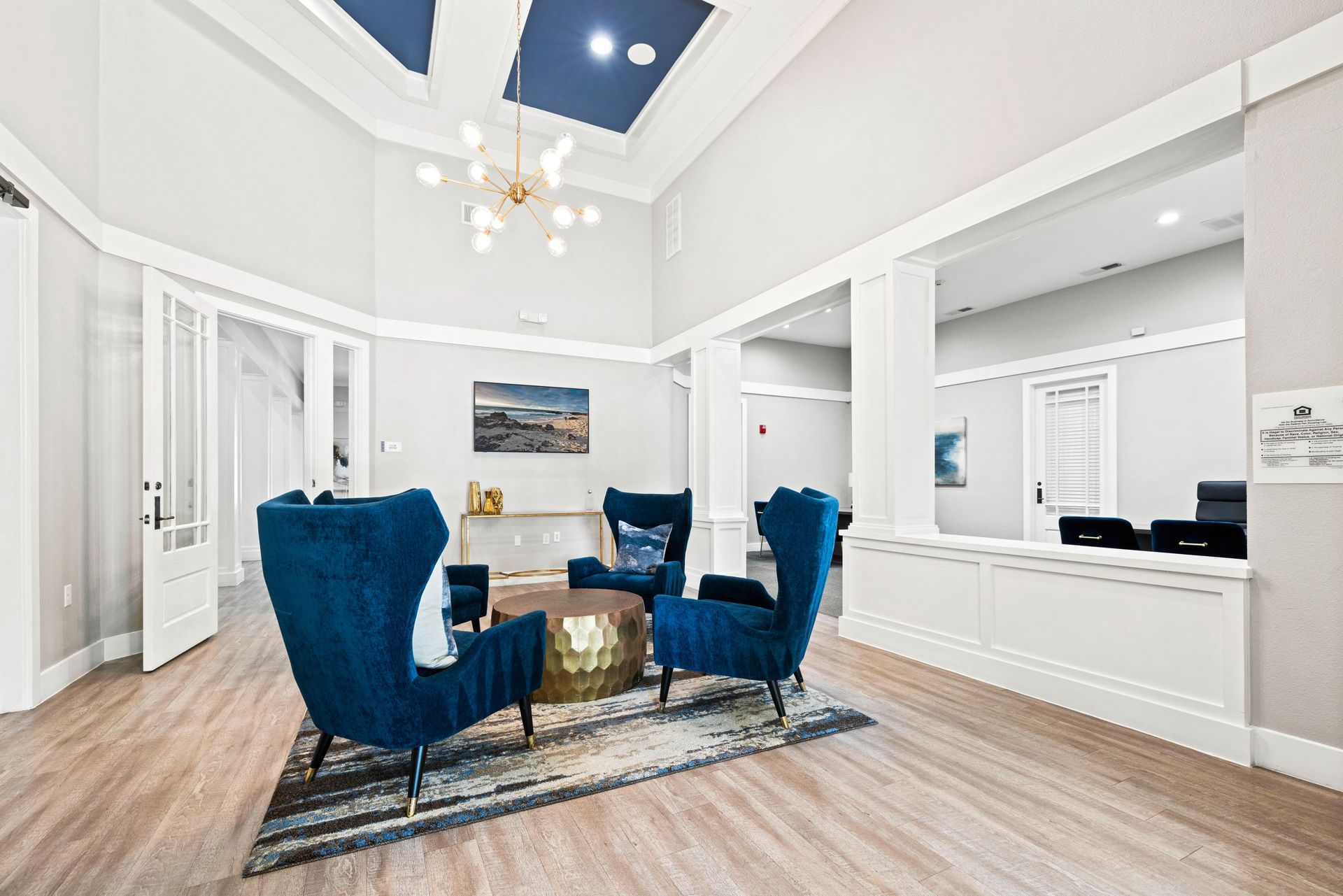 Bright modern living room with blue chairs, white walls, wood floors, and a high vaulted ceiling