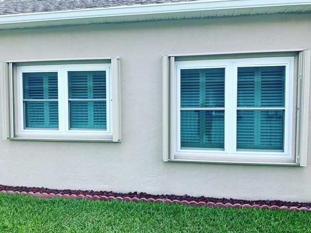 Two windows on the side of a house with green shutters