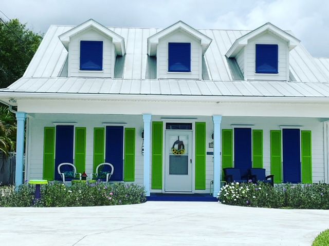 A white house with green shutters and blue windows