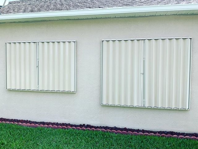 Two windows on the side of a house with shutters on them