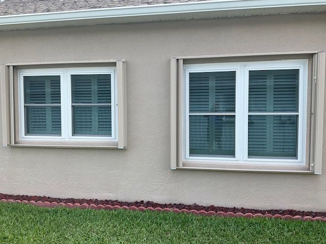 Two windows on the side of a house with white shutters