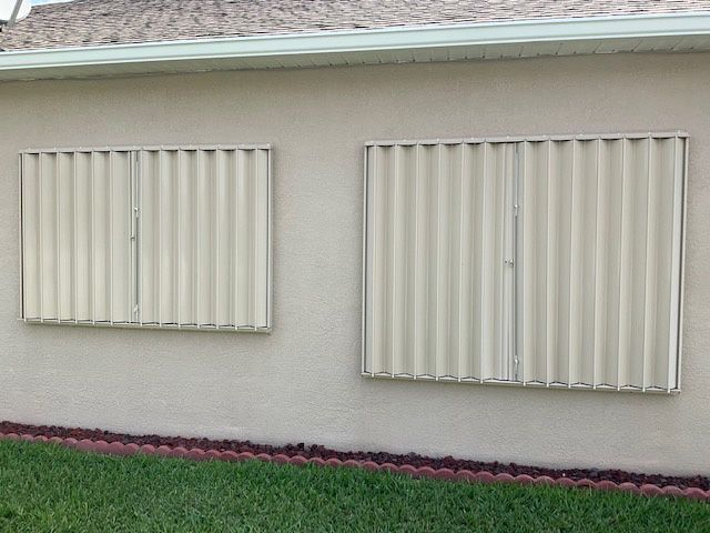 Two windows on the side of a house with shutters on them
