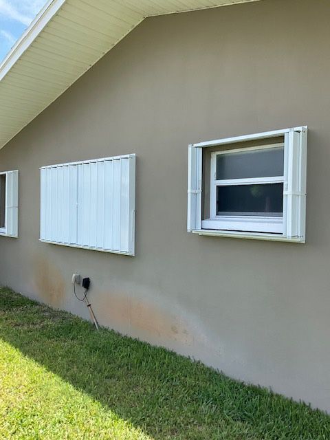 Two windows on the side of a house with white shutters
