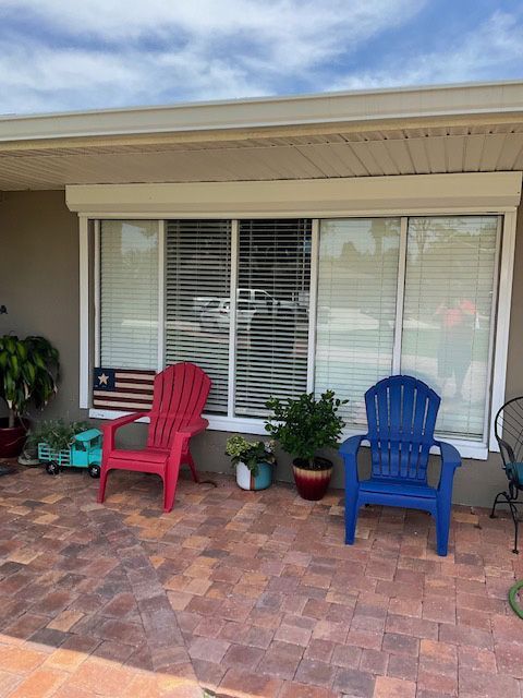 A red chair and a blue chair sit on a patio in front of a window