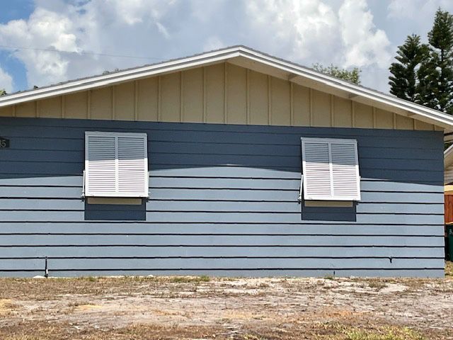 A blue and tan house with shutters on the windows is sitting on top of a dirt field