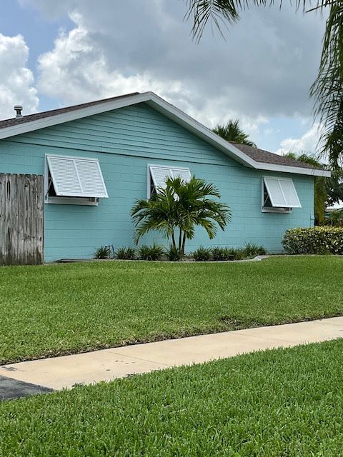 A blue house with white awnings on the windows is sitting on top of a lush green lawn.