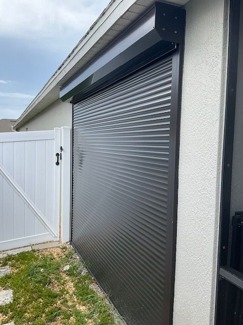 A black garage door is sitting next to a white gate on the side of a house