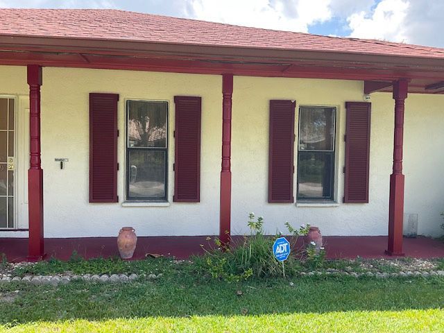 A white house with red shutters and a red roof is for sale