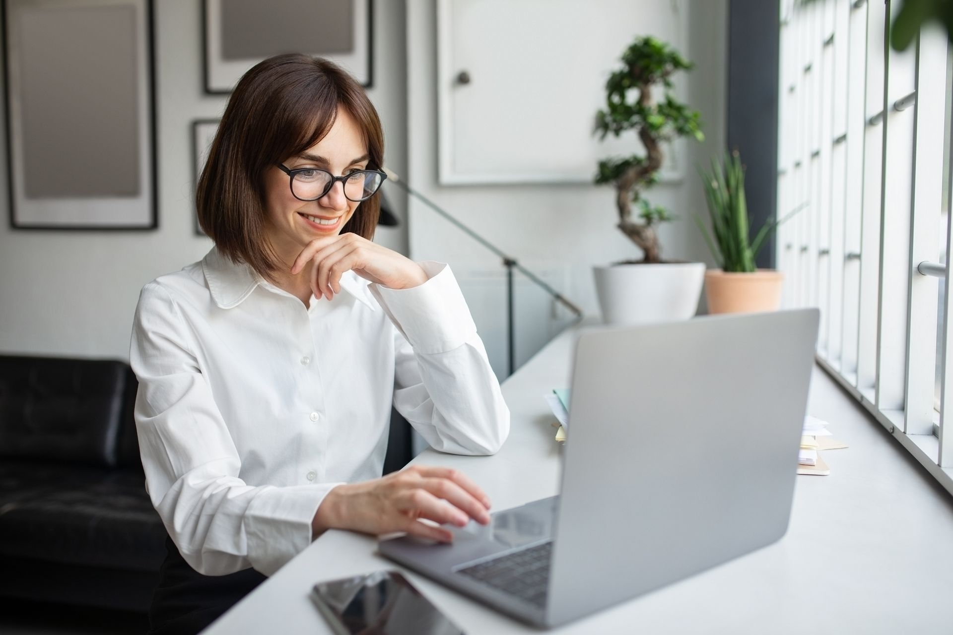 A woman is sitting at a desk on a live stream call on  a laptop computer.