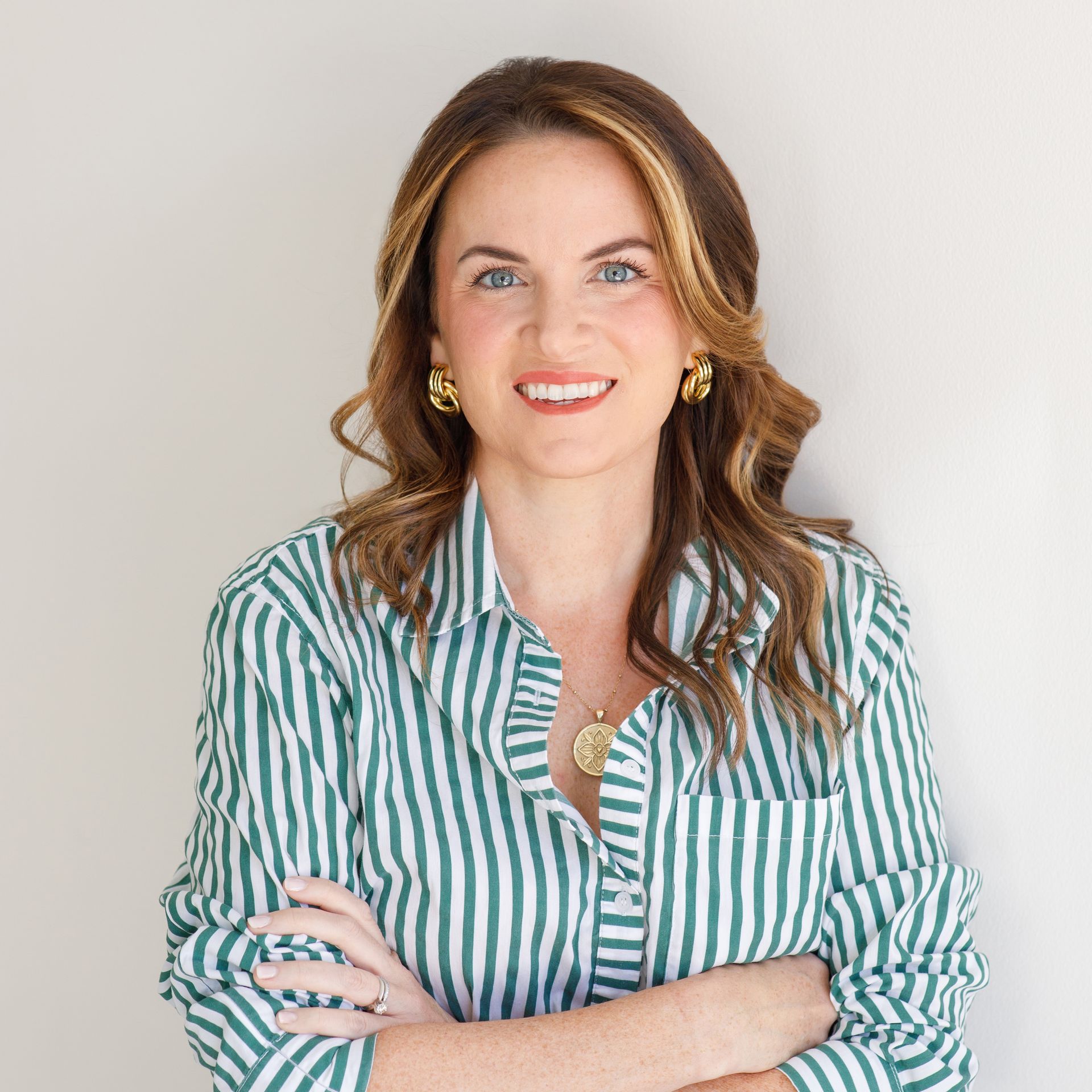 A woman wearing a pink jacket and earrings is smiling for the camera.