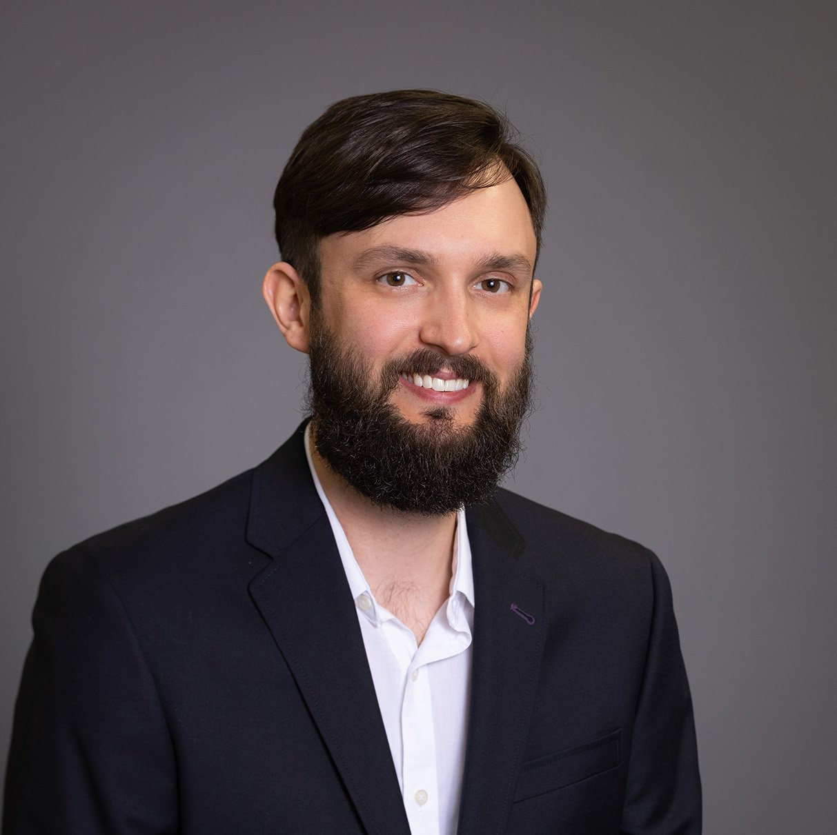 A man with a beard is wearing a suit and smiling for the camera.