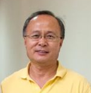 A man wearing glasses and a yellow shirt is standing in front of a white wall.