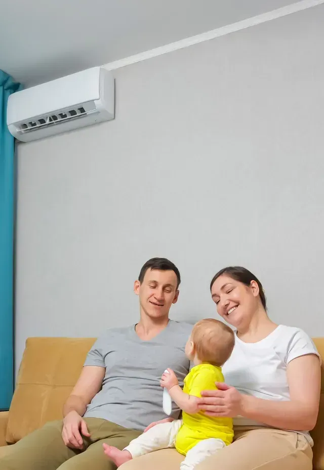 A family is sitting on a couch under an air conditioner.