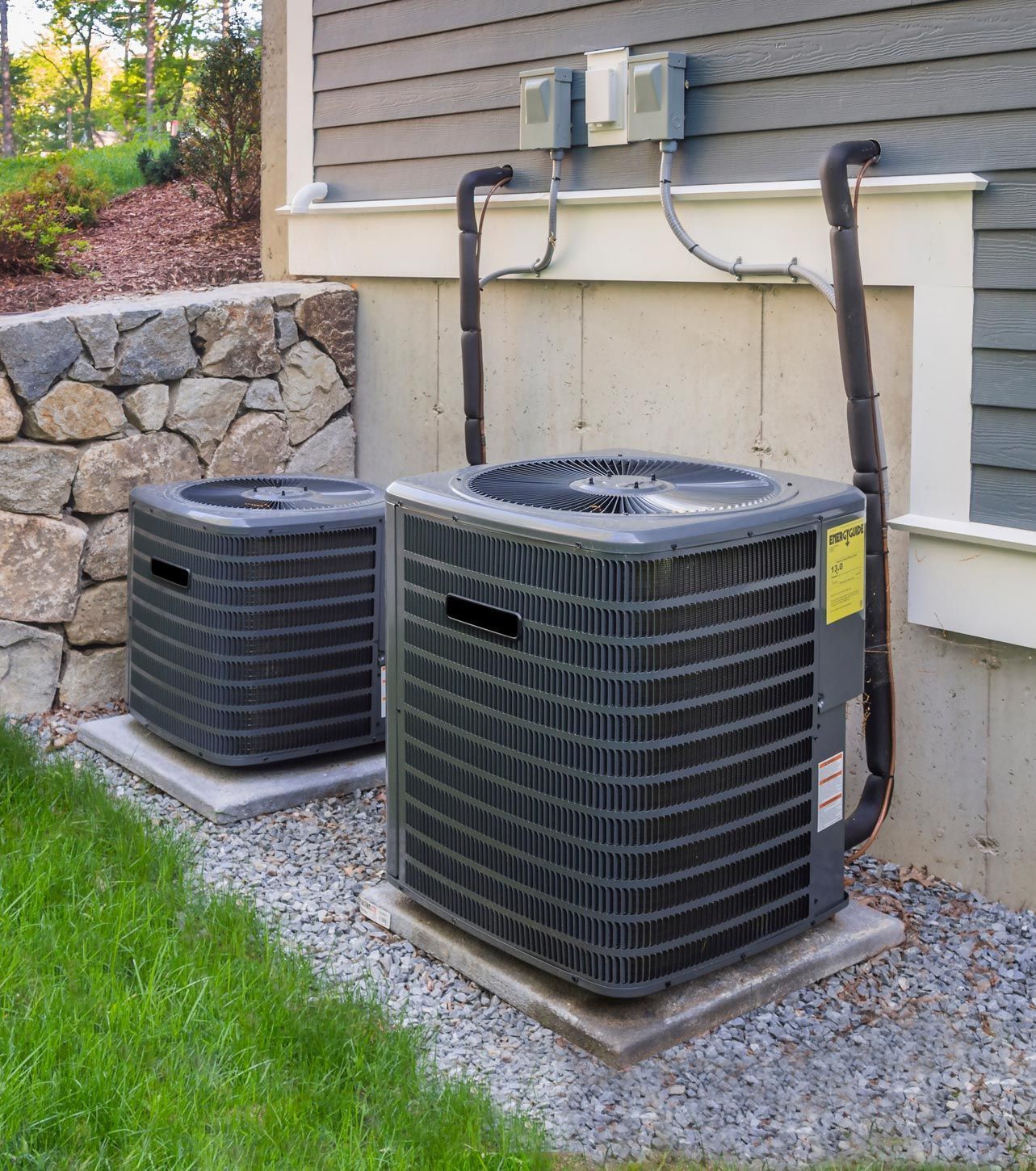 Two air conditioners are sitting outside of a house