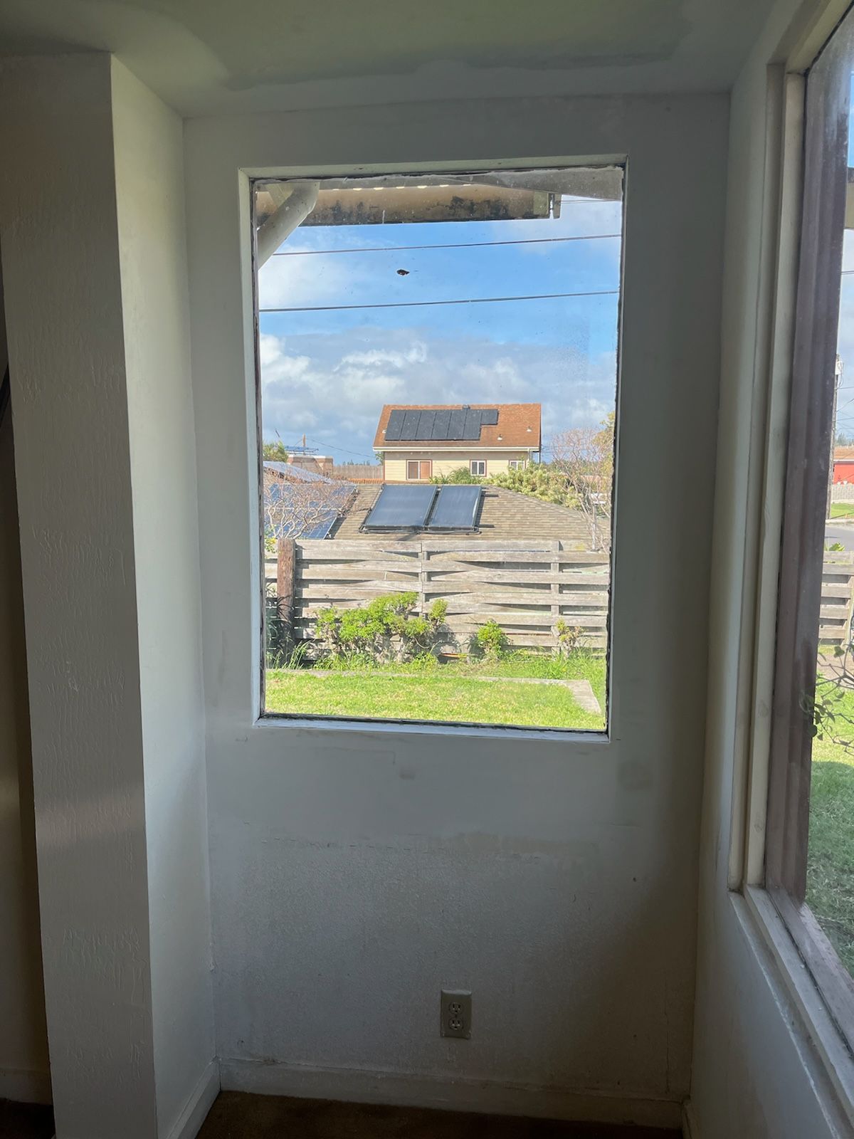 Window looking out onto a backyard with a fence and a house with solar panels.