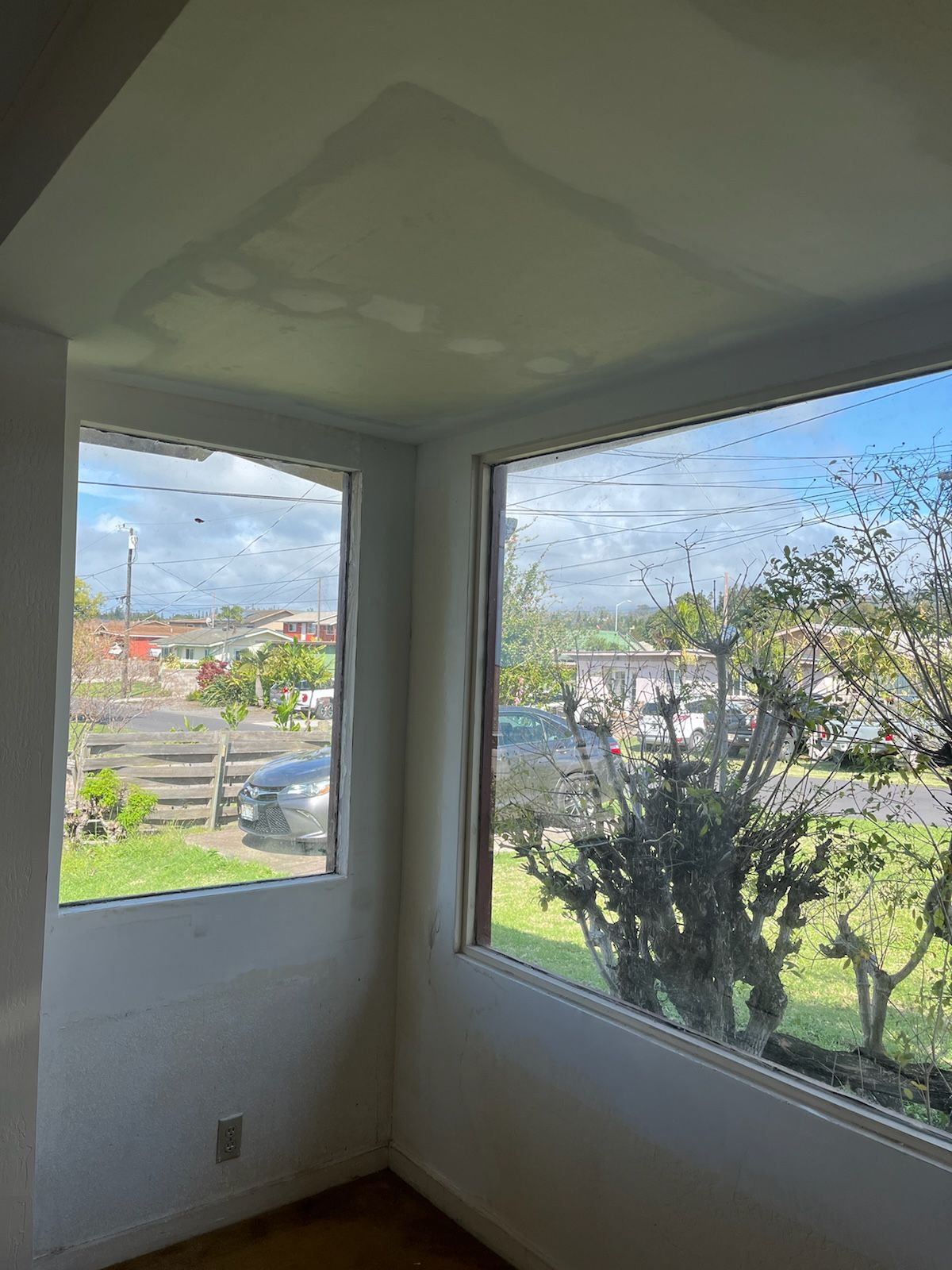 Corner room with two windows showing neighborhood view; water damage on ceiling.