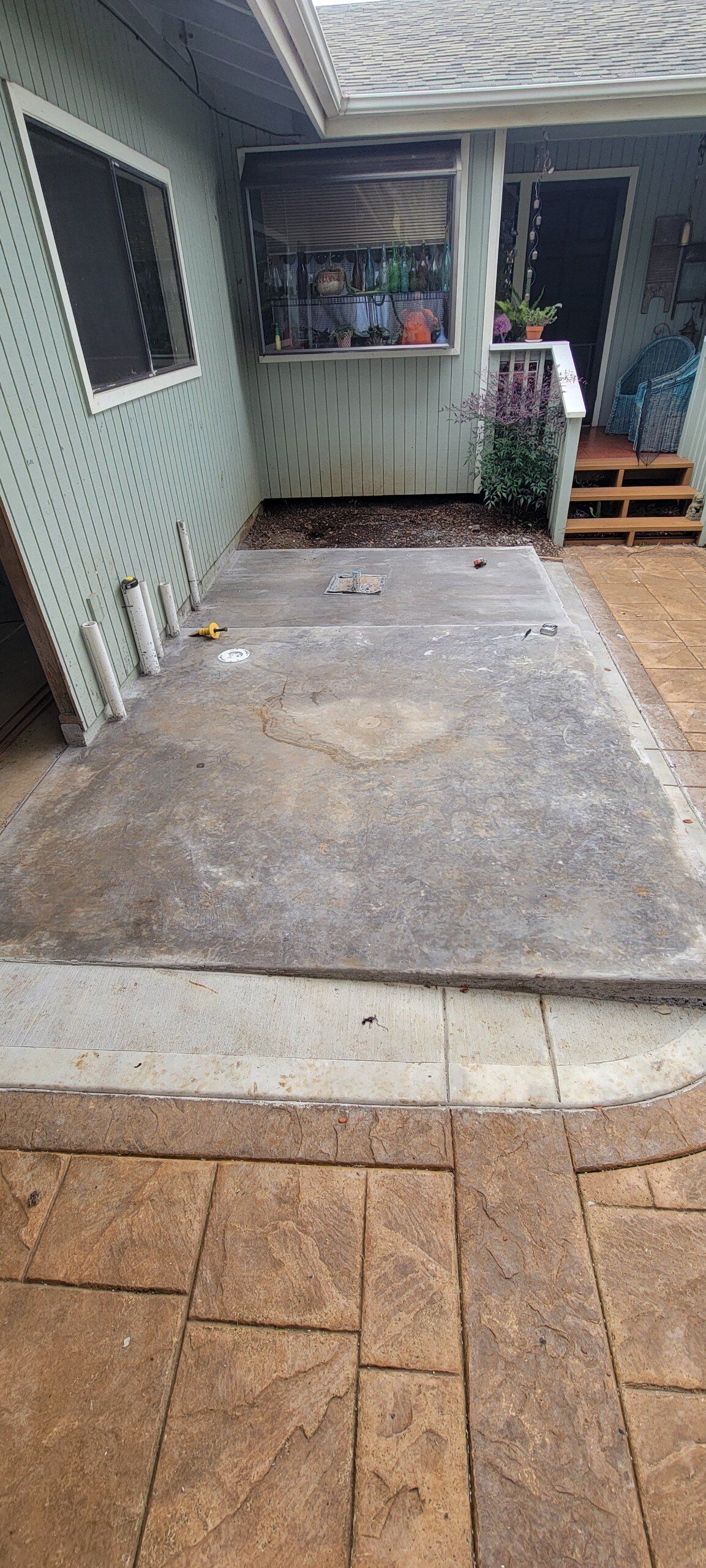 Exterior patio with concrete and stone pavers leading to a doorway. Light green house with a window.