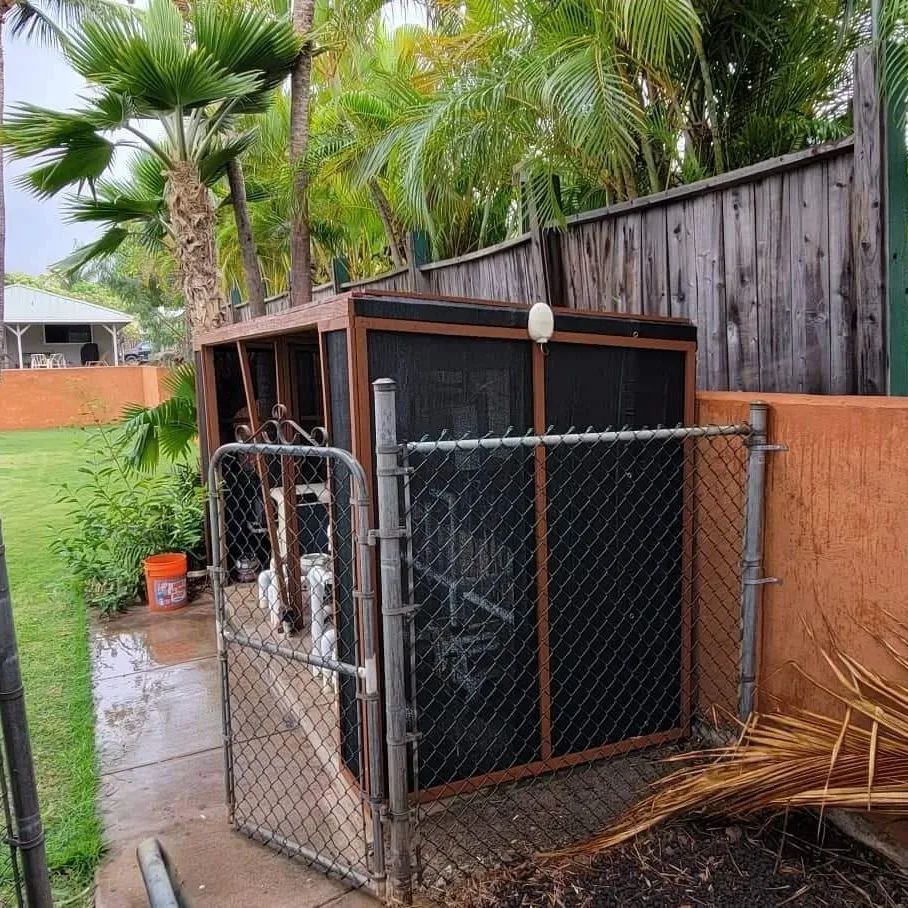 Pool equipment enclosure with a black mesh front, chain-link gate, and surrounding greenery.