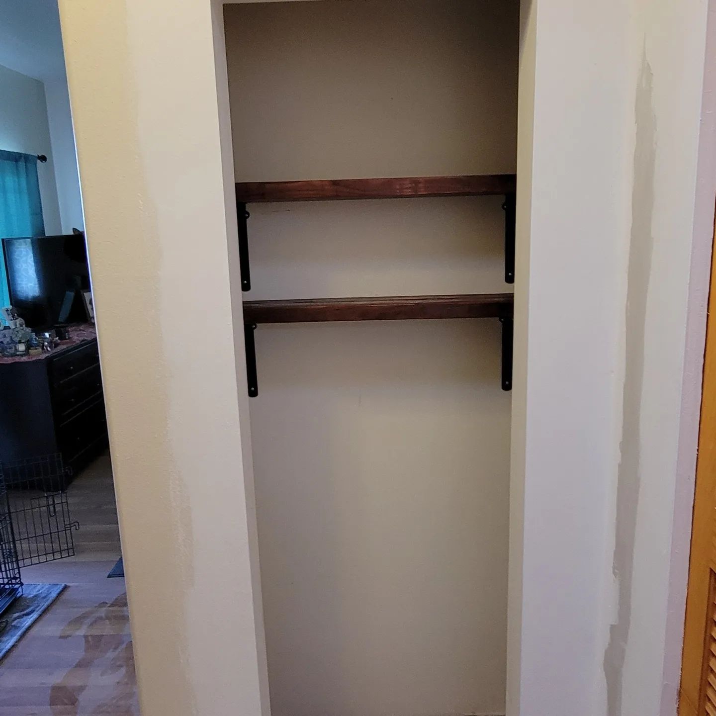 Built-in closet with two wooden shelves supported by black brackets. Cream walls and light brown shelving.