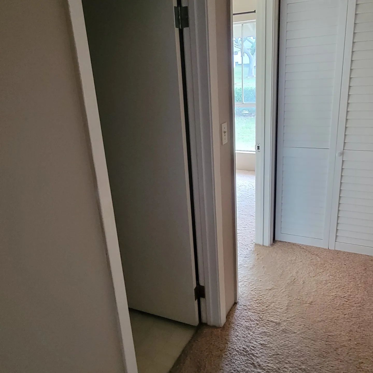 Hallway with open door to a room with window, carpet, and closet doors.