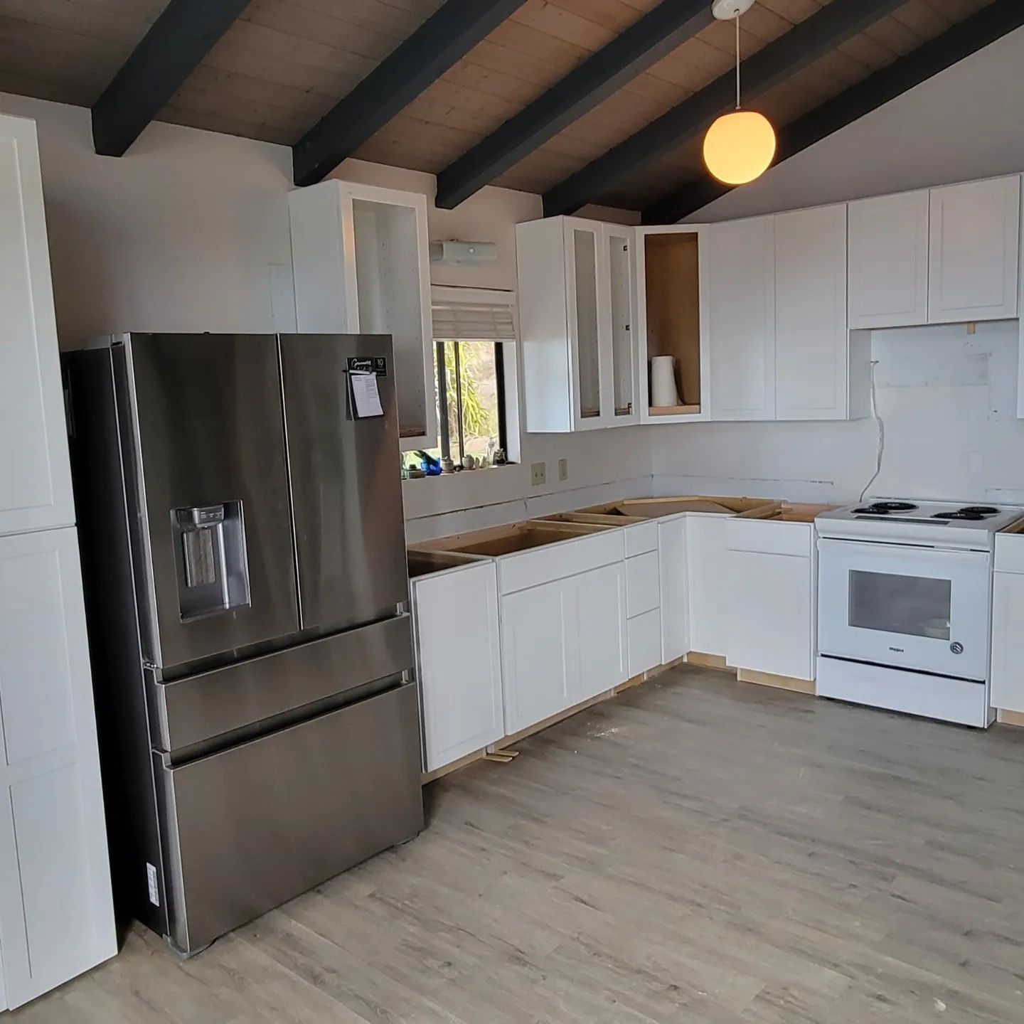 Kitchen under renovation with white cabinets, stainless steel refrigerator, and unfinished countertops.