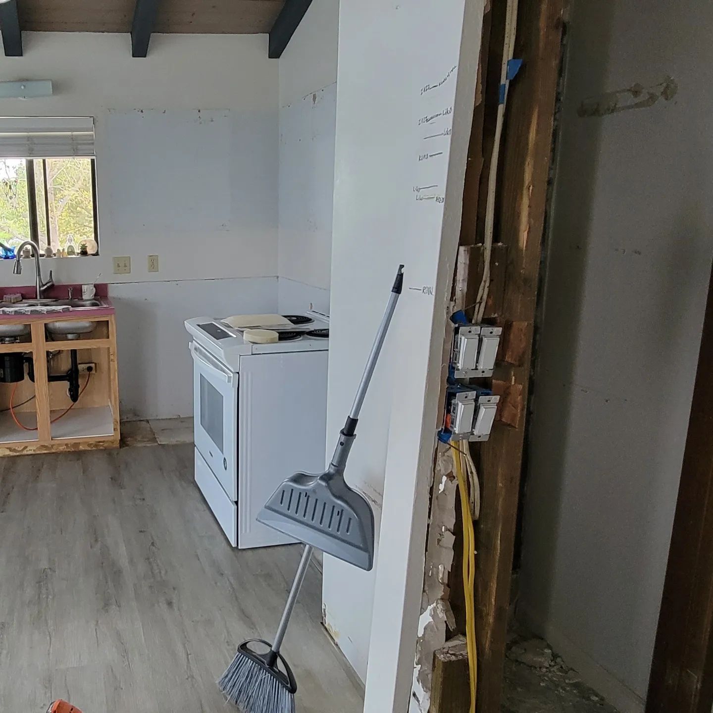 Kitchen undergoing renovation. White appliances, partially exposed wall, broom and dustpan.