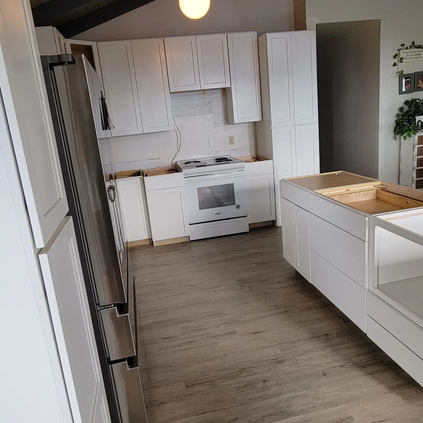 Kitchen under renovation: White cabinets, island, and appliances, wood-look flooring.