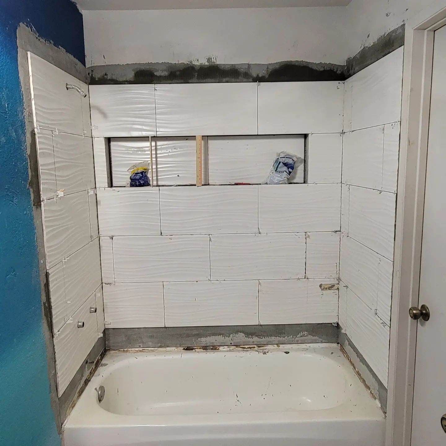 Bathroom under renovation with white tub and tiled walls in progress.