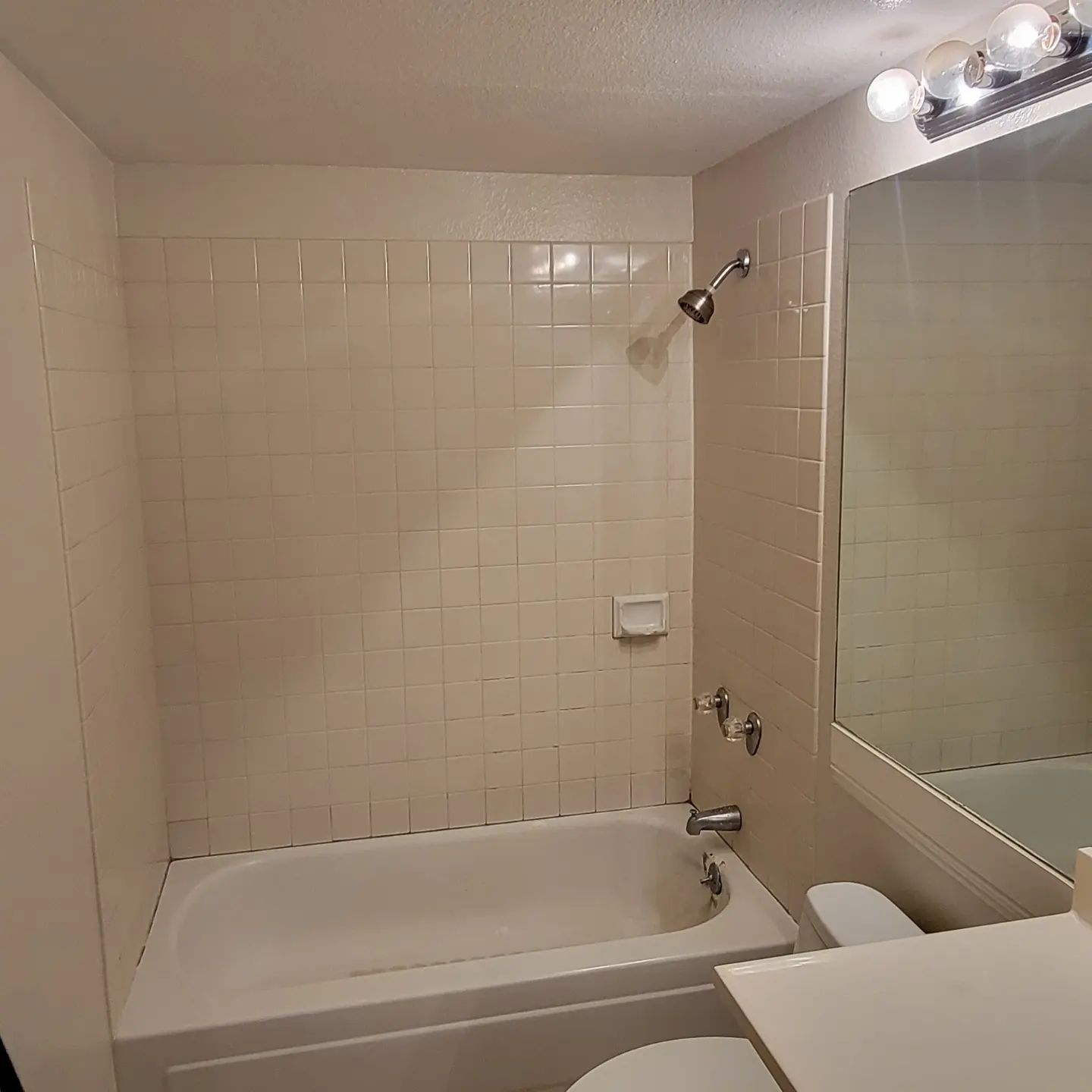 Bathroom with a white bathtub, tiled walls, and a mirror.