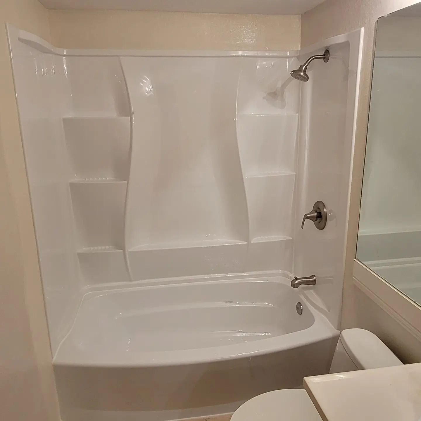 White alcove bathtub and shower with shelves, chrome fixtures, and toilet.
